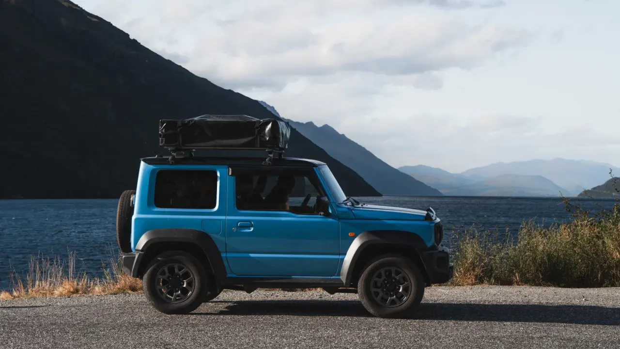 Suzuki Jimny on snowy gravel track with snow-capped mountains. – Jimny Rentals.