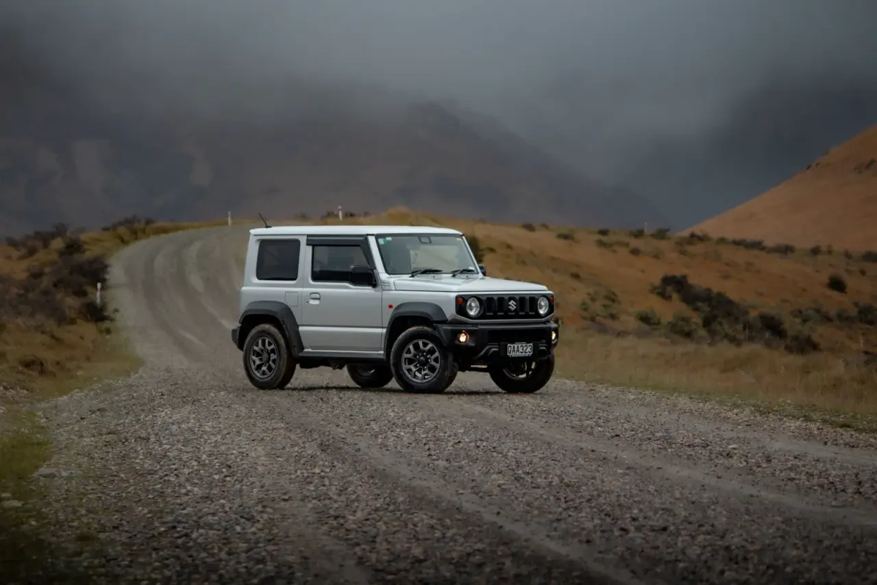 Suzuki Jimny with rooftop tent on gravel road, mountain views. – Jimny Rentals.